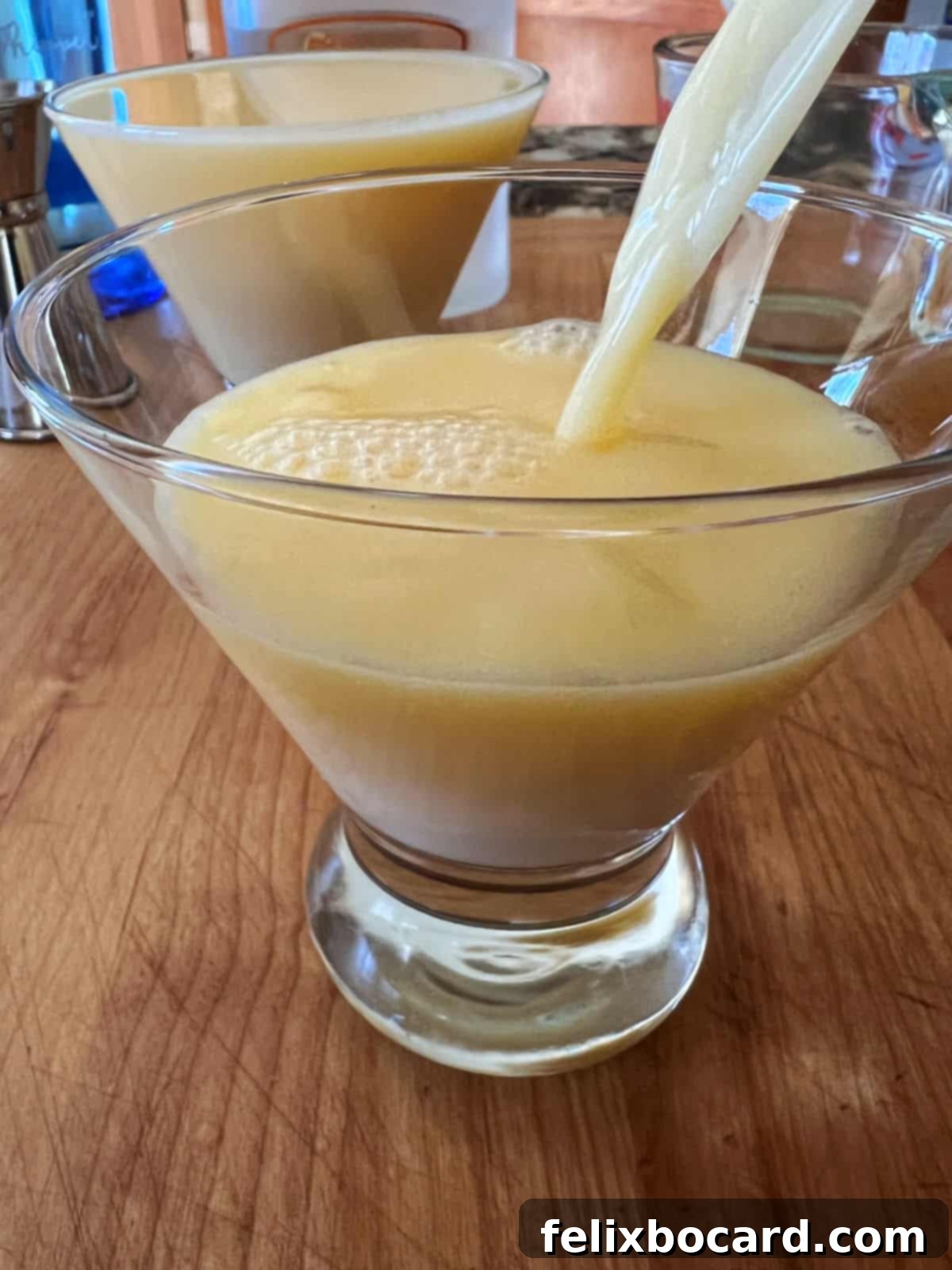 A vibrant Orange Creamsicle Cocktail being strained from a cocktail shaker into a stylish stemless martini glass, showing the smooth liquid filling the glass.