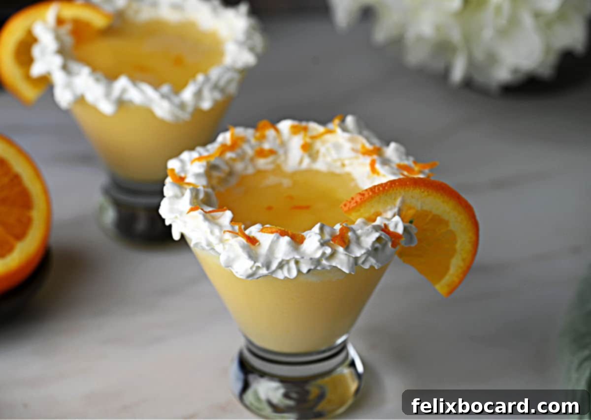 Two beautifully presented Orange Creamsicle Cocktails in martini glasses, each topped with a lavish swirl of whipped cream, fresh orange zest, and a vibrant half-orange slice.
