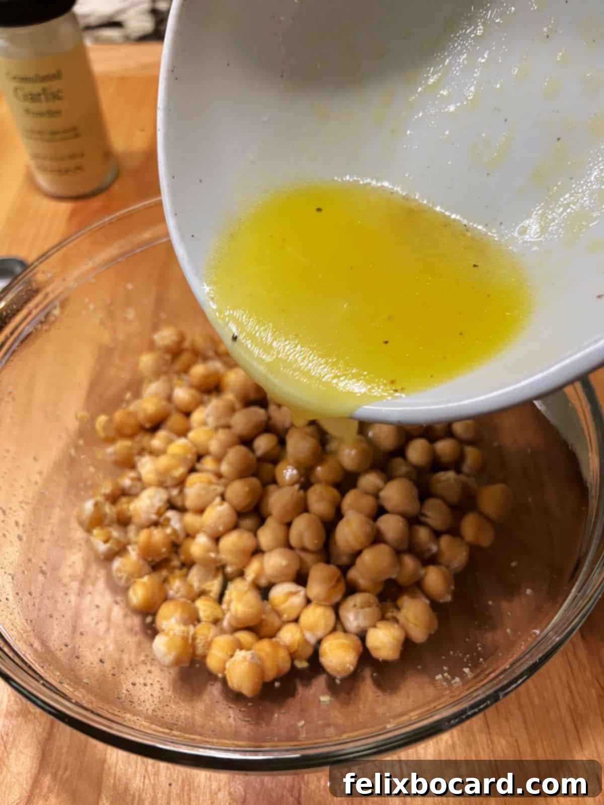 Pouring the freshly prepared lemon and olive oil dressing over a bowl of warm, microwaved chickpeas, ready for marination.