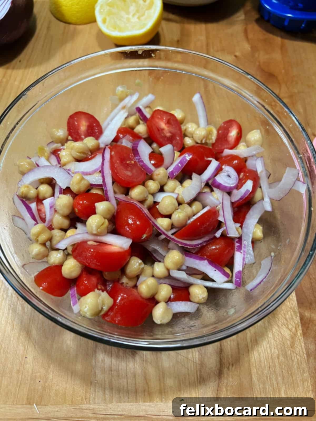 A close-up view of the marinated chickpeas, halved grape tomatoes, and sliced red onion, perfectly mixed in a bowl, waiting for the final addition of avocado.