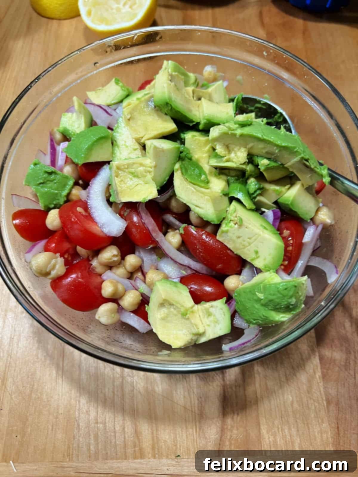 Freshly diced avocado cubes added to the mixed chickpea, tomato, and onion salad, enhancing its creaminess and nutritional value.