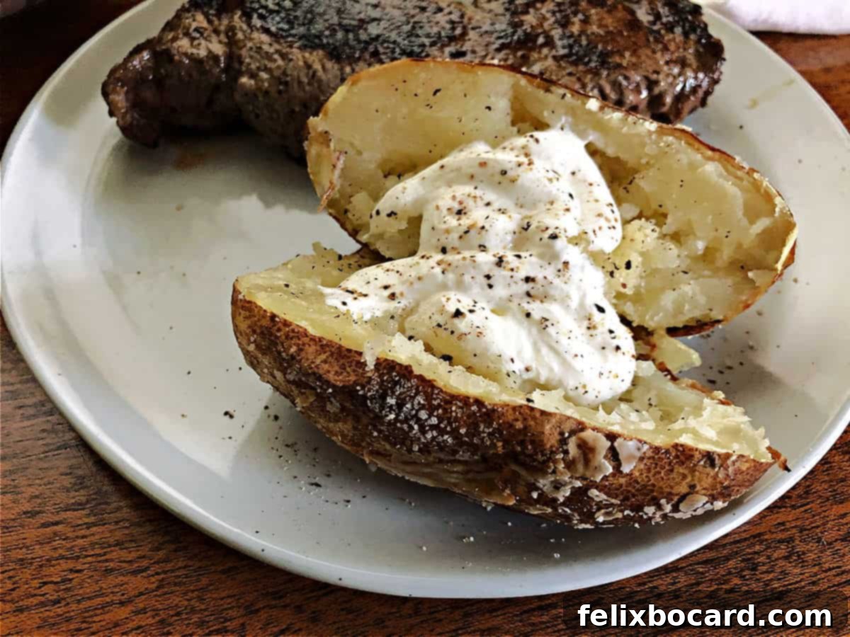 Perfectly grilled baked potato on a plate, garnished with sour cream, alongside a steak