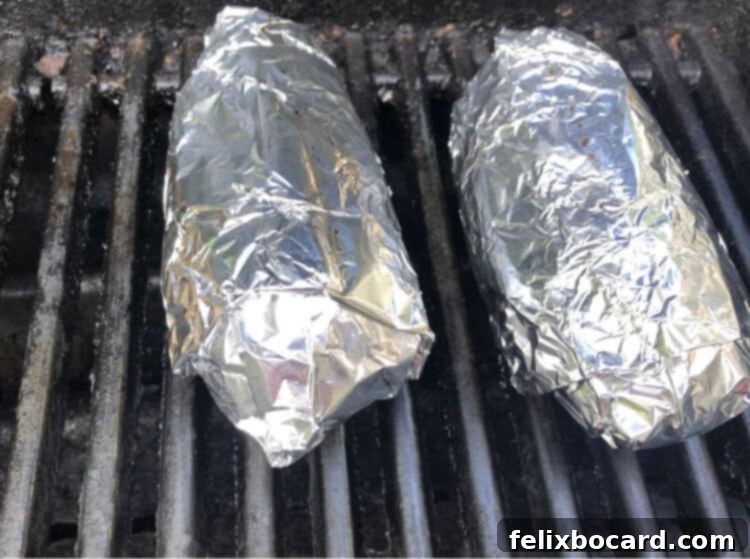 Foil-wrapped potatoes resting on hot black grill grates, ready for cooking
