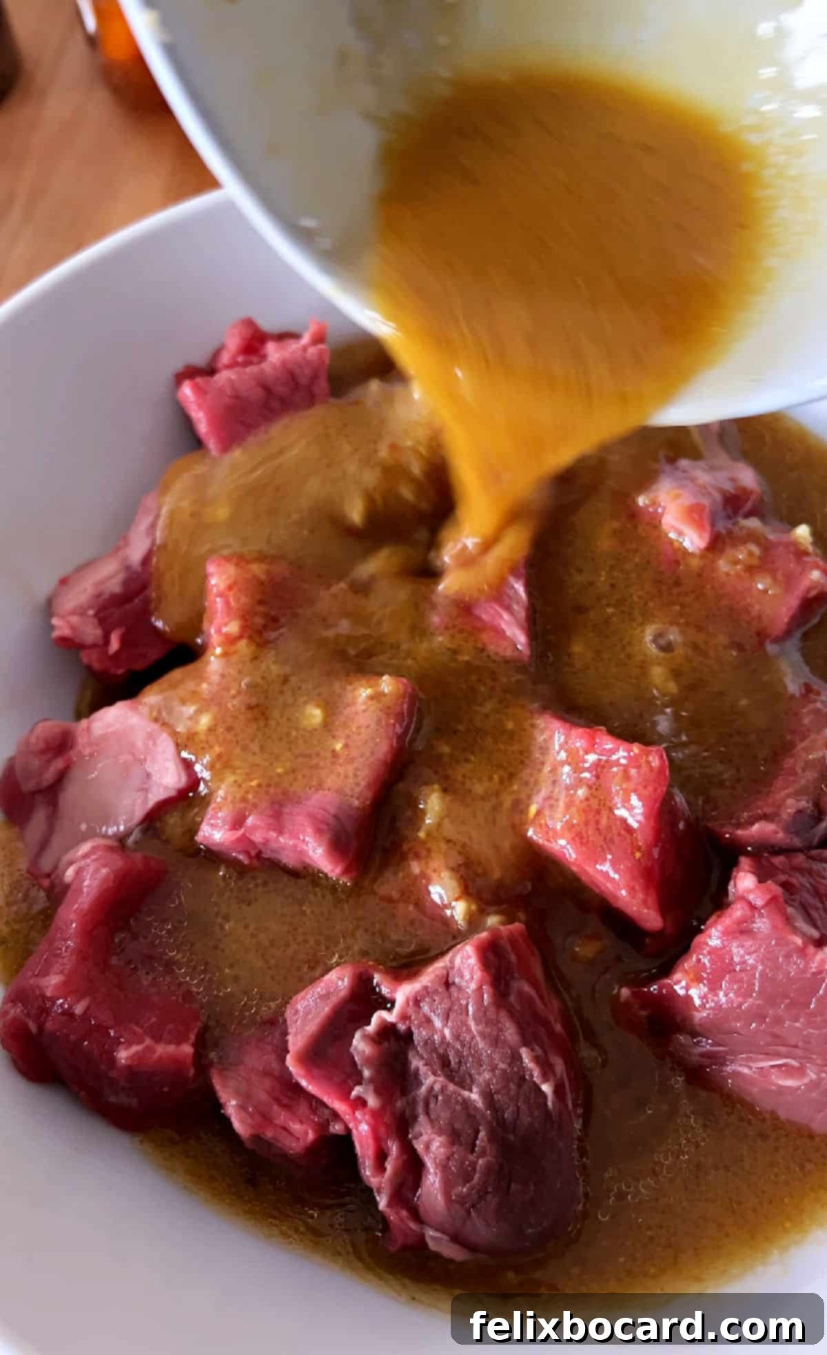 Chef pouring homemade beef kabob marinade over cubed beef in a bowl, ensuring thorough coating before marinating.