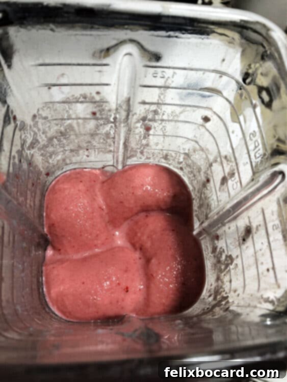 A top-down view of a vibrant smoothie being blended in a high-speed blender, creating a creamy texture.
