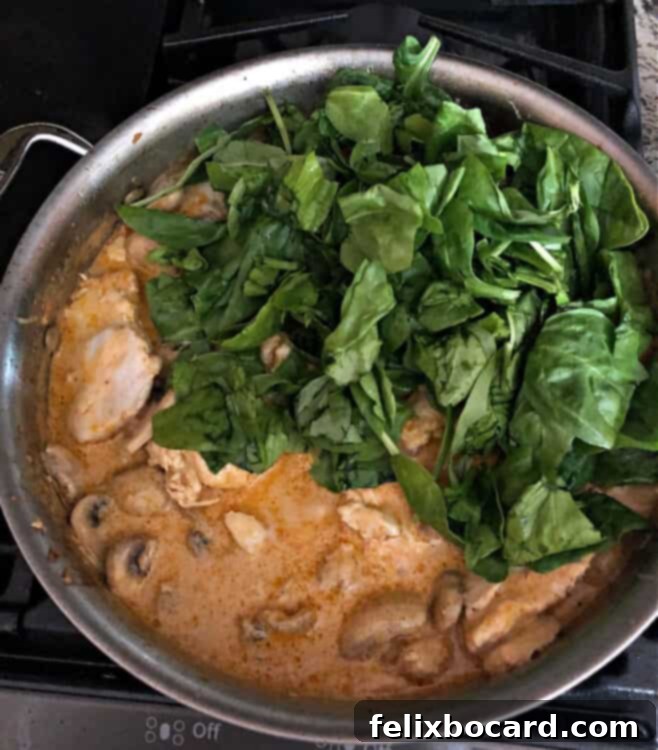 Sun dried tomato pesto chicken in a pan, adding fresh spinach