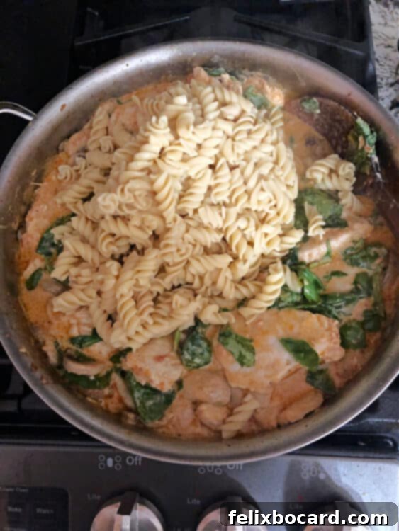 Adding cooked pasta noodles directly to the pan of creamy sun-dried tomato pesto chicken sauce