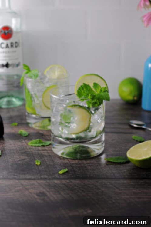 Two glasses of Bacardi Mojitos, garnished with fresh mint and lime, surrounded by mint leaves.