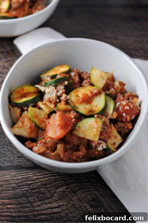 A serving of the delicious zucchini casserole with ground beef in a pristine white bowl, showcasing its rich texture and melted cheese.