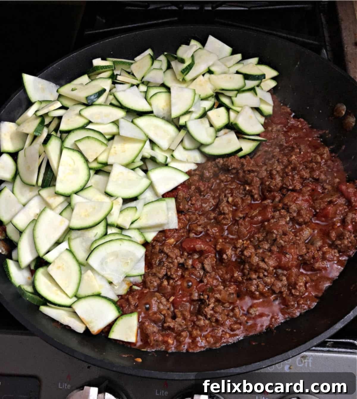 Sliced zucchini being added to a large skillet containing a seasoned ground beef and tomato mixture, ready to be combined.