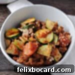 A small white bowl filled with ground beef zucchini casserole, artfully placed on a white napkin.