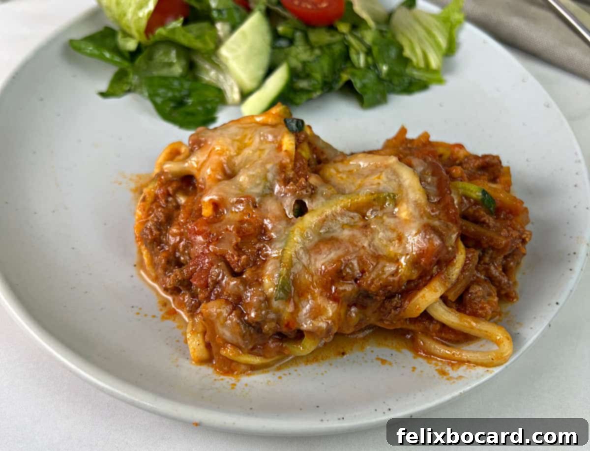 A serving of butternut squash and zucchini spaghetti bake on a plate with salad, showcasing a healthy, low-carb meal.