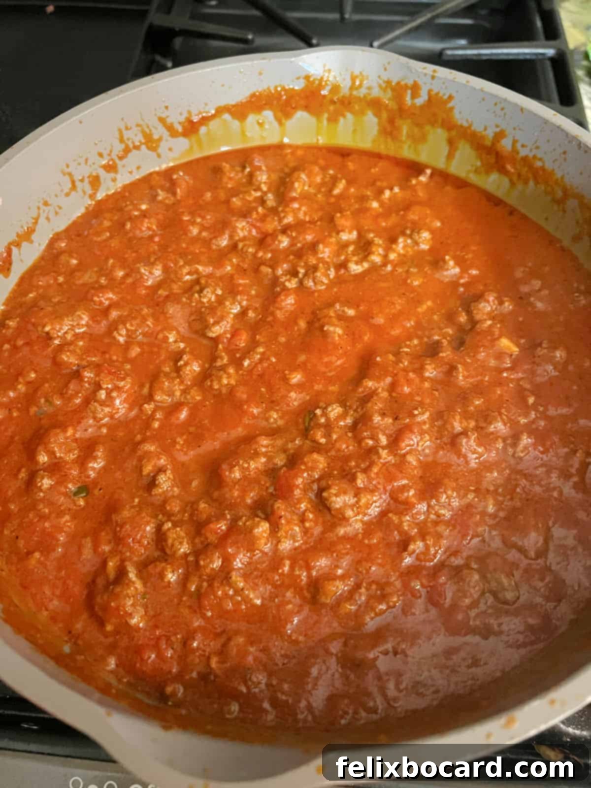 Meat and marinara sauce simmering in a large pan on the stove, creating a rich spaghetti base.