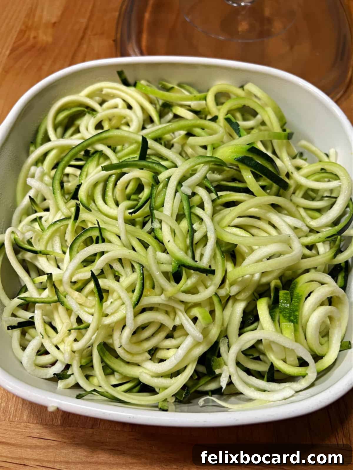 Fresh zucchini noodles (zoodles) in a microwave-safe bowl, ready for pre-cooking.