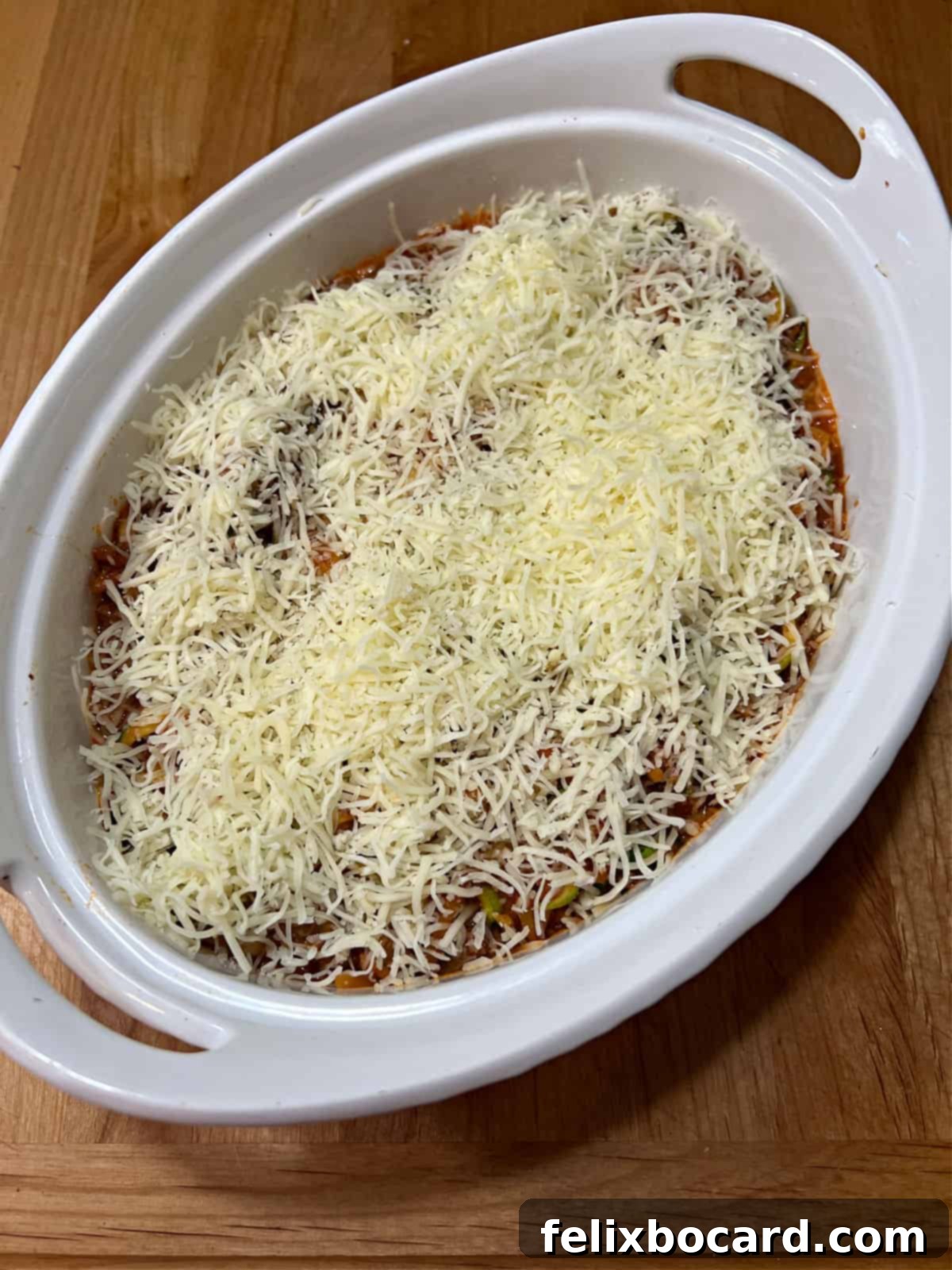The butternut squash and zucchini spaghetti mixture placed in a casserole dish, topped with a generous layer of shredded cheese.