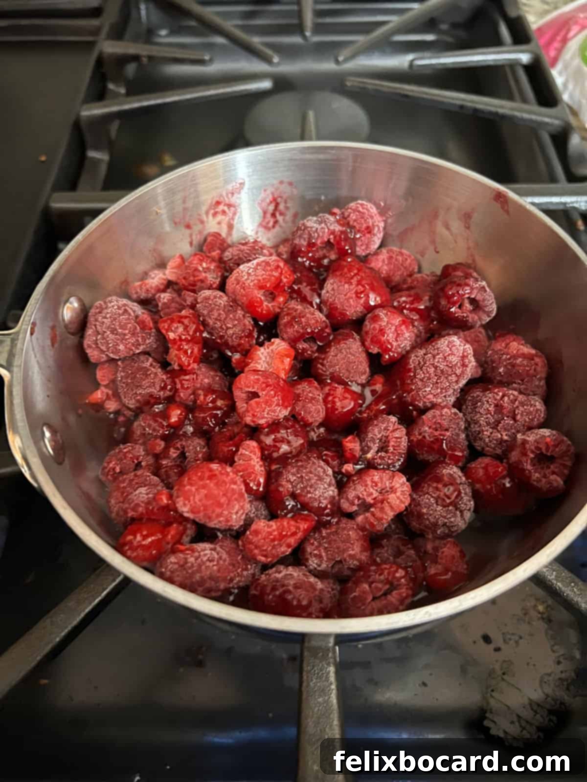 Frozen raspberries and sugar-free jam starting to cook together in a small saucepan.