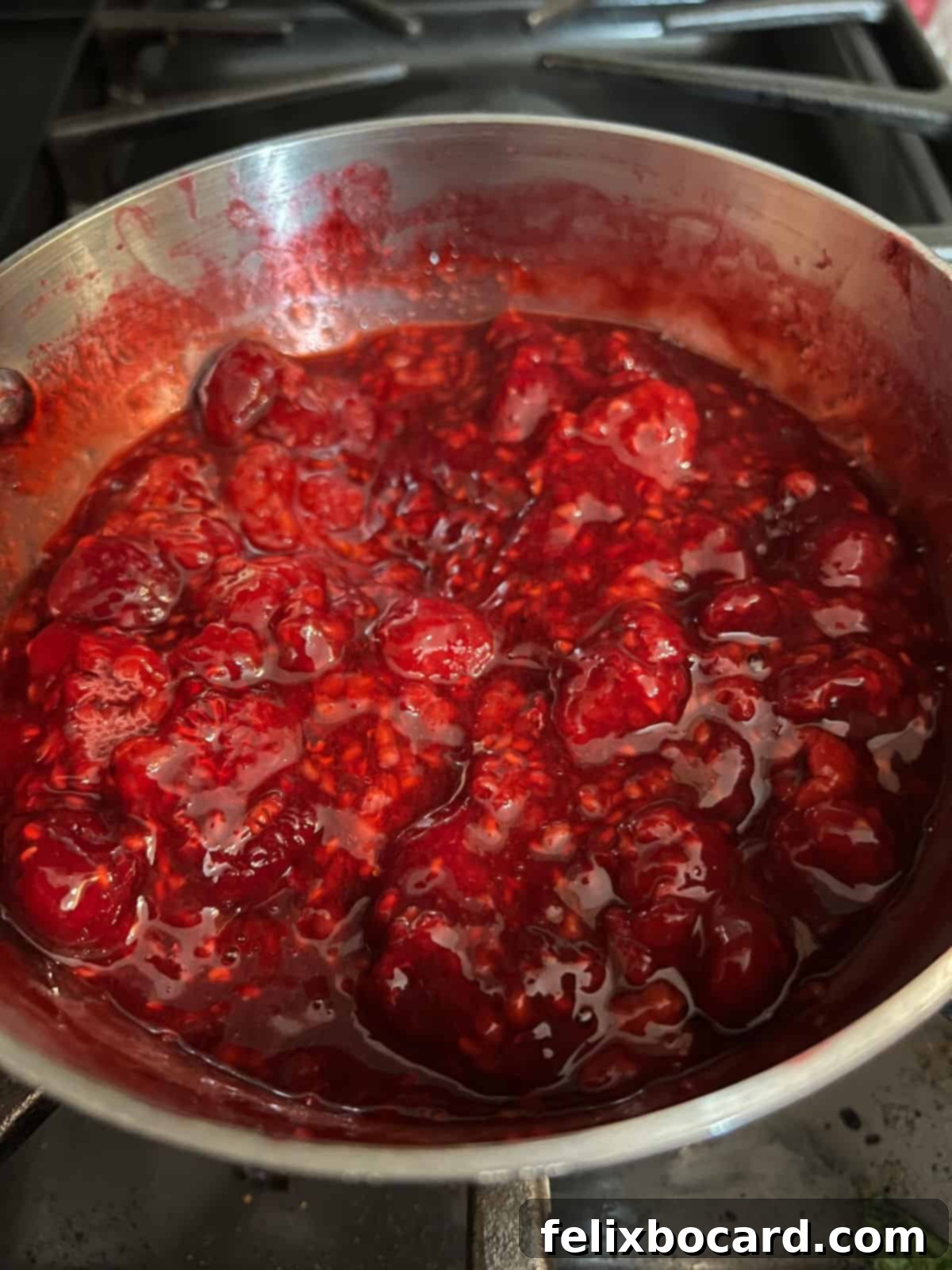 Keto raspberry sauce actively cooking on a stovetop, with berries softening in the jam.