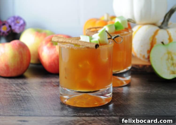 Caramel Apple Vodka Indulgence 2 Two caramel apple cider cocktails with whole apples and small pumpkins in the background, set for autumn.