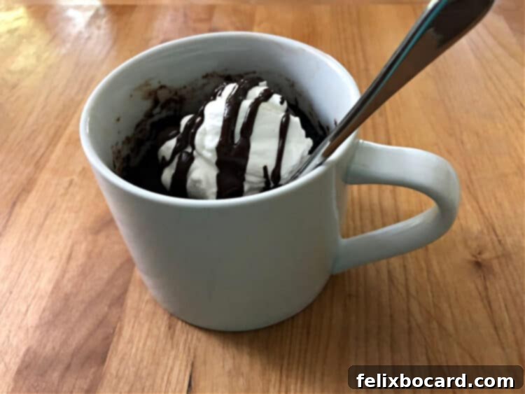keto chocolate mug cake with whipped cream and drizzled chocolate, a spoon sticking out of the mug