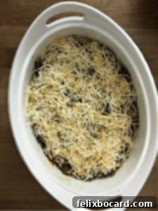 Keto Taco Casserole before baking, showing the layers of seasoned meat, egg, and shredded cheese in a casserole dish.