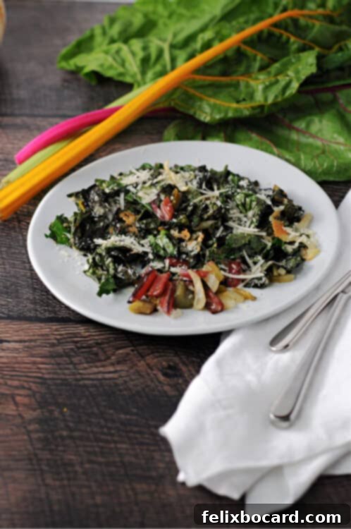 A small white plate holds a serving of golden-brown roasted Swiss chard with melted Parmesan, alongside some fresh chard in the background.