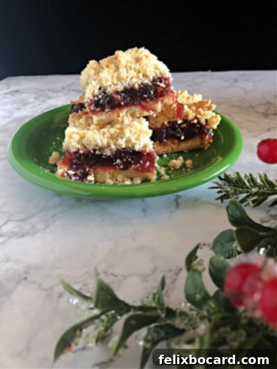 Plate of cranberry bars behind some Christmas greens and holly, suggesting a festive occasion.