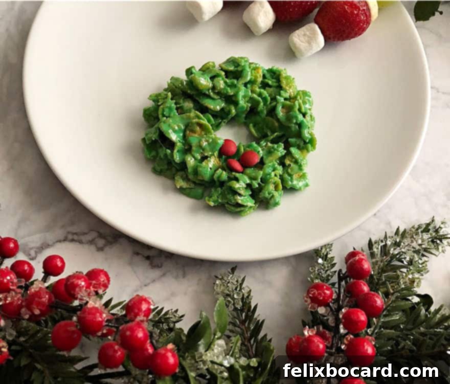 Vibrant green Cornflake Marshmallow Cookie Wreath decorated with bright red candies, resting on a clean white surface, embodying festive holiday cheer.