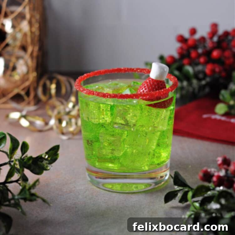 Grinch cocktail on the rocks in a glass rimmed with red sugar, featuring a strawberry and marshmallow garnish.