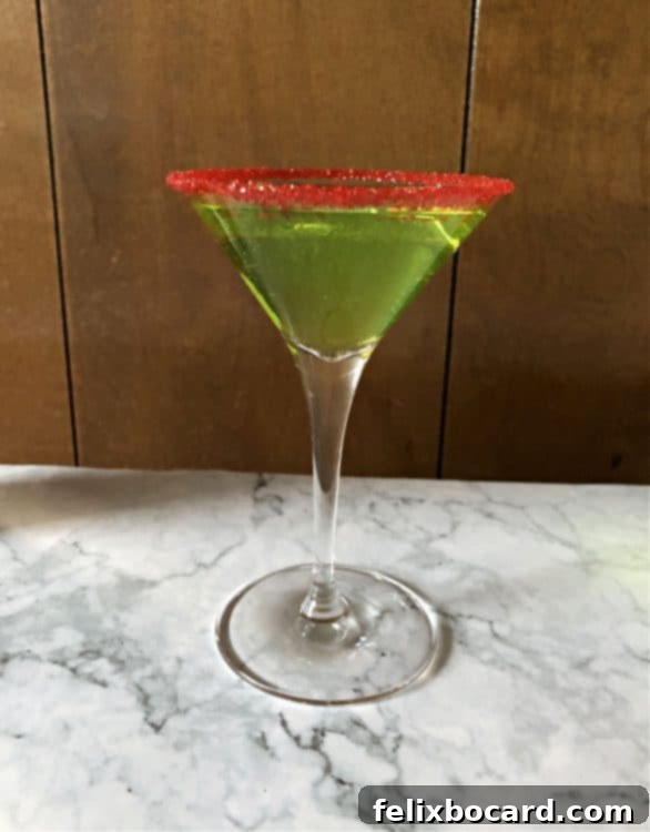 Martini glass with a red sugar rim and a vibrant green Grinch cocktail.