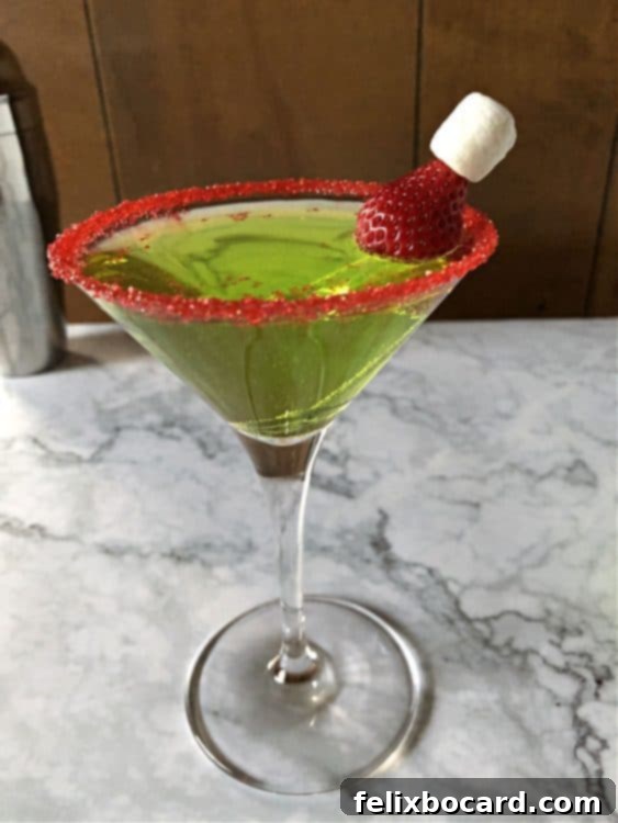 Grinch cocktail garnished with a strawberry and marshmallow Santa hat.