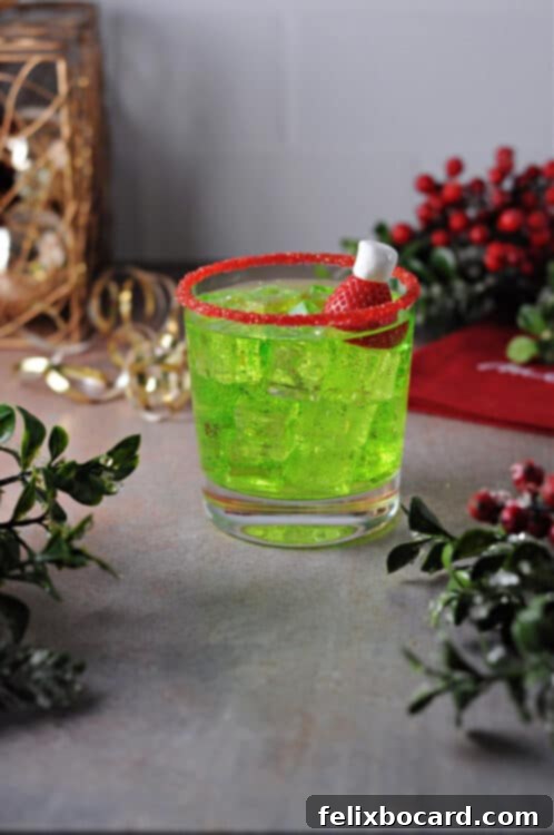 Grinch cocktail served on the rocks, garnished with a strawberry Santa hat and a red sugar rim.