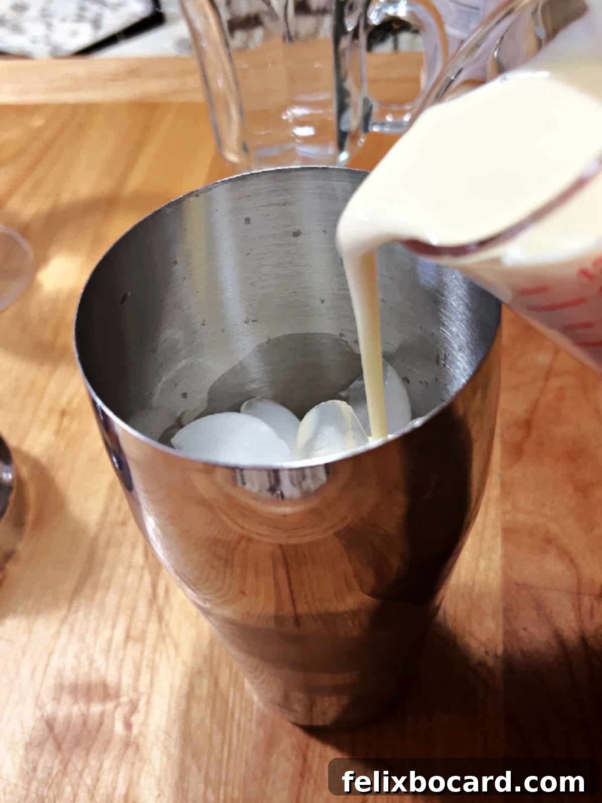A close-up shot of a cocktail shaker being filled with ice and the liquid ingredients for an Eggnog Baileys cocktail, preparing for mixing.