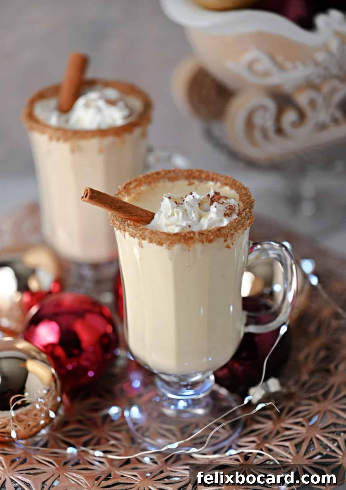 A beautifully garnished Eggnog Baileys cocktail in a coupe glass, topped with whipped cream, grated nutmeg, and a cinnamon stick, evoking holiday cheer.