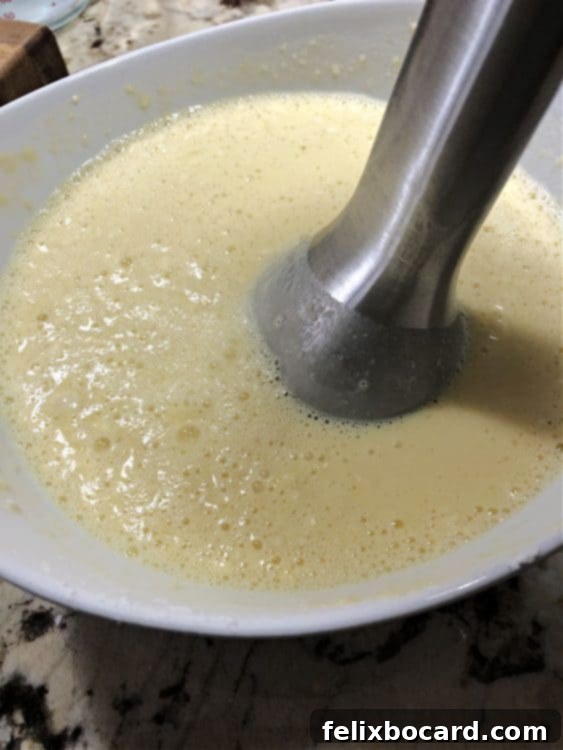 Immersion blender being used in a bowl of crepe batter to achieve a smooth consistency.