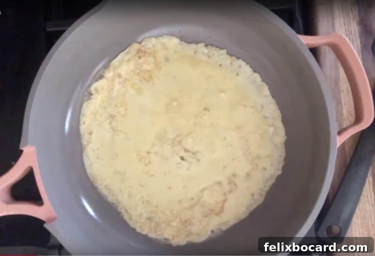 Thin crepe batter cooking evenly in a non-stick skillet, forming delicate edges.