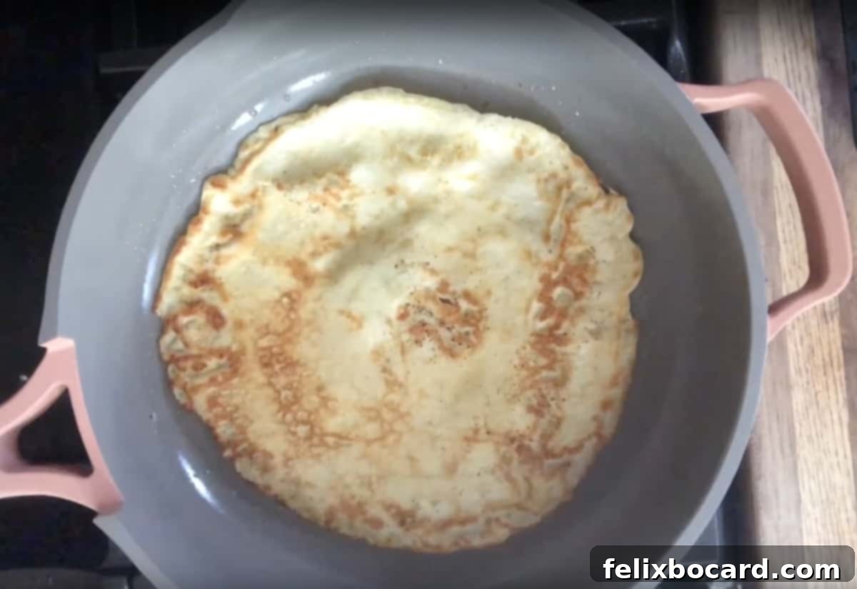 A crepe perfectly flipped in a pan, with the cooked side showing a golden hue and the uncooked side sizzling.
