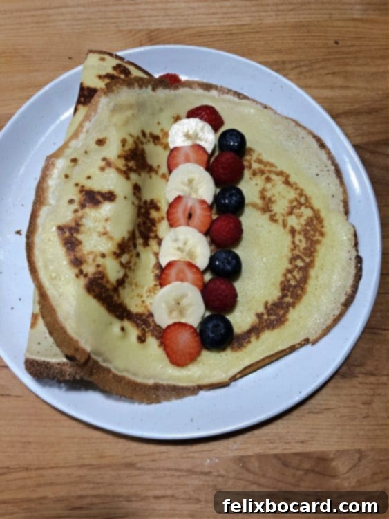 Crepe adorned with a colorful line of fresh fruit filling, including berries and banana slices.