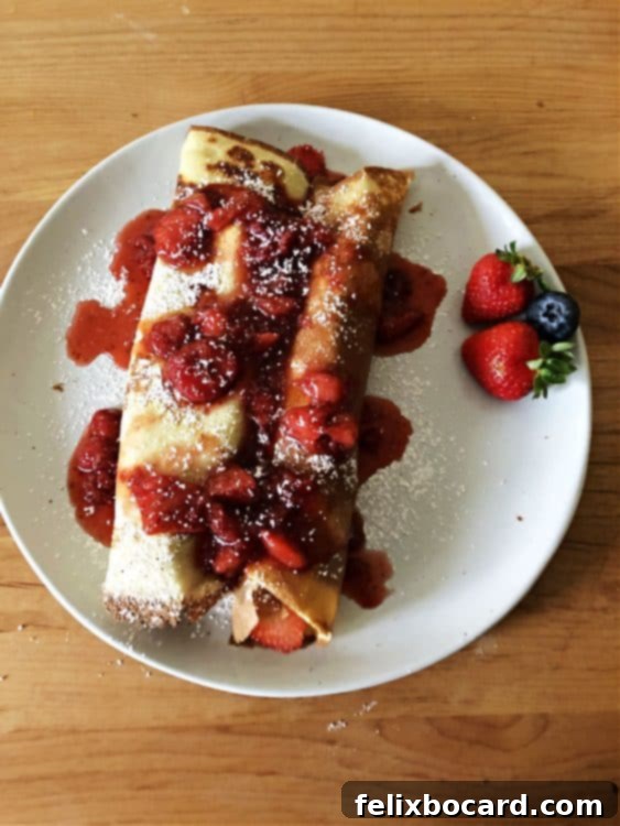 Rolled-up fruit crepe drizzled with a rich berry sauce, showcasing a delectable presentation.
