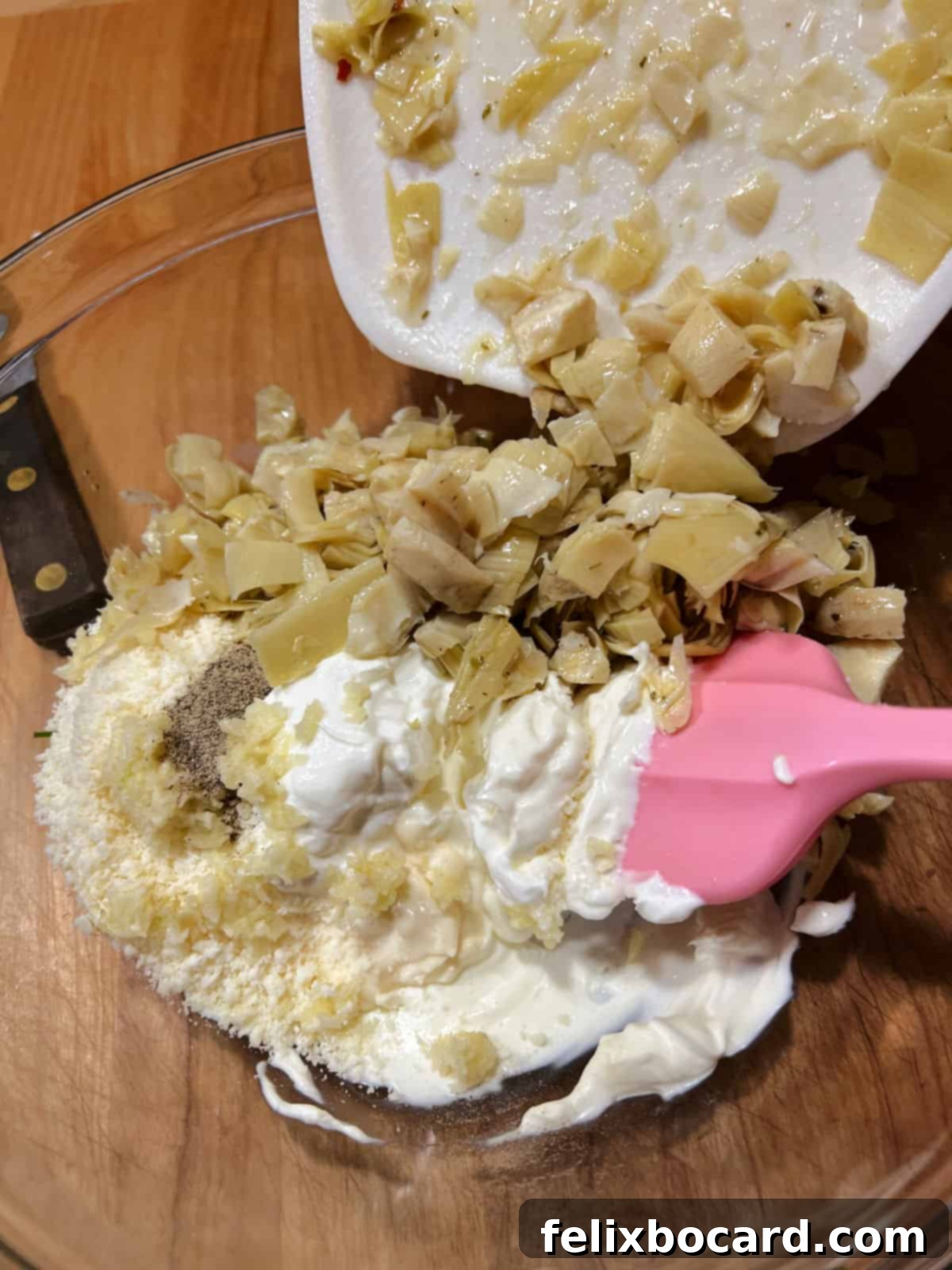Various dip ingredients being added to a large mixing bowl, including cream cheese, mayonnaise, and other components.