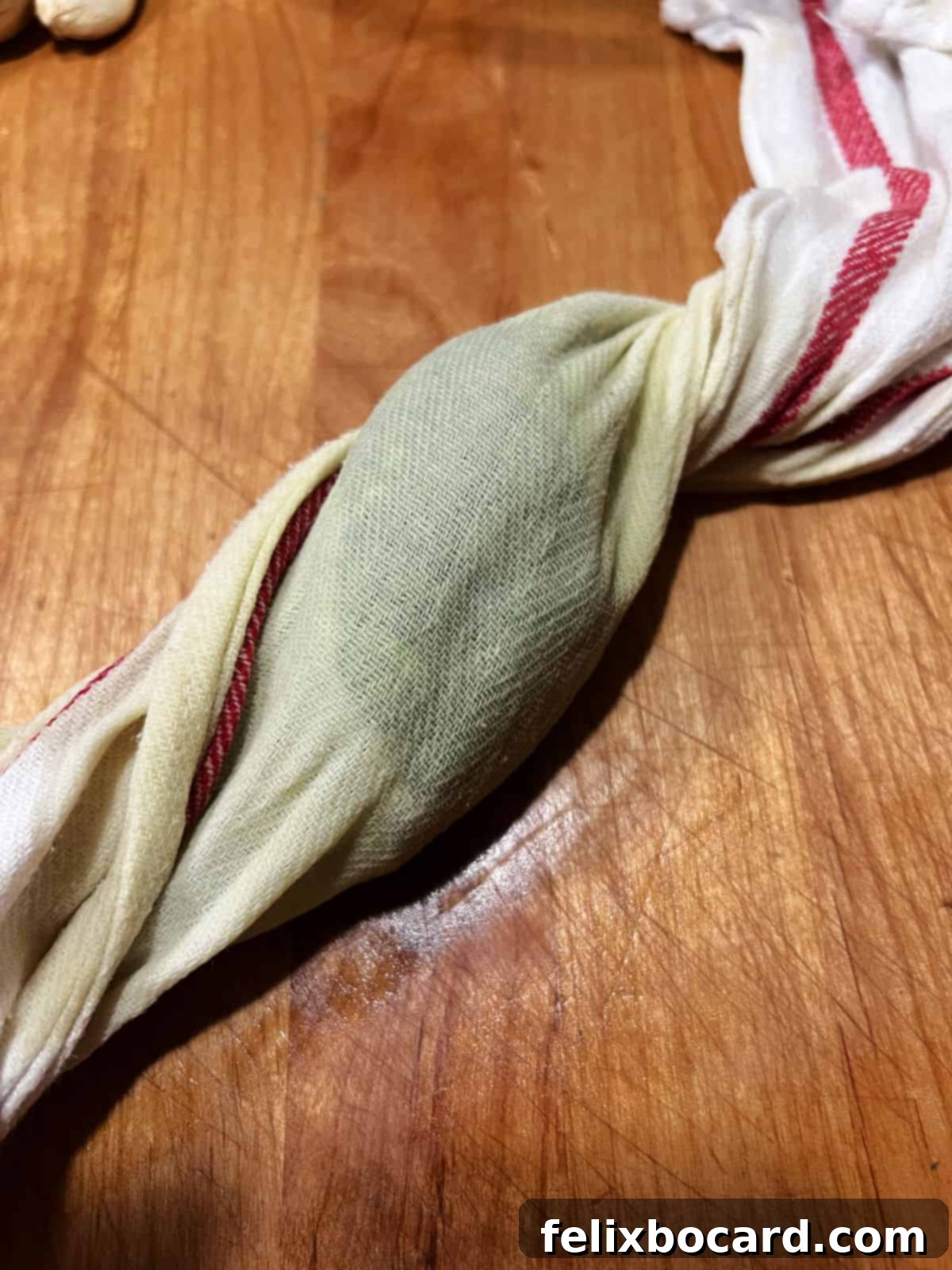 Hands twisting a kitchen towel filled with wilted spinach to extract excess moisture, demonstrating a crucial step for a creamy dip.
