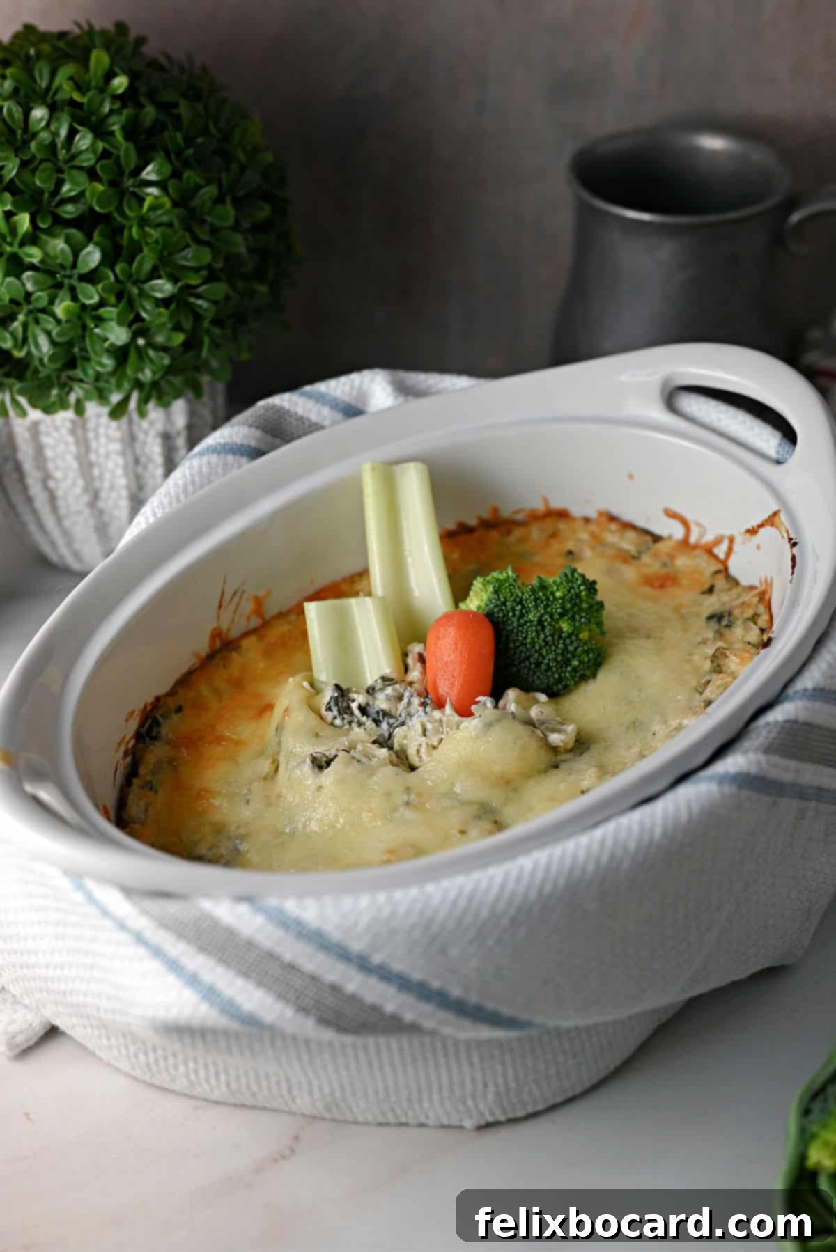 Baked keto spinach artichoke dip with various vegetable sticks like celery and carrots arranged around it for dipping.