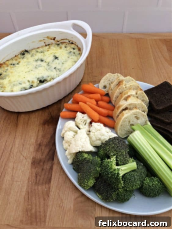 Spinach artichoke dip displayed next to a plate featuring a variety of breads, crackers, and fresh vegetables for dipping.