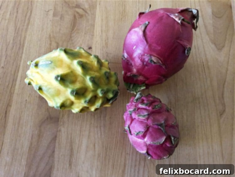 Three different varieties of whole dragon fruit, uncut, showcasing their distinct skin colors and shapes.