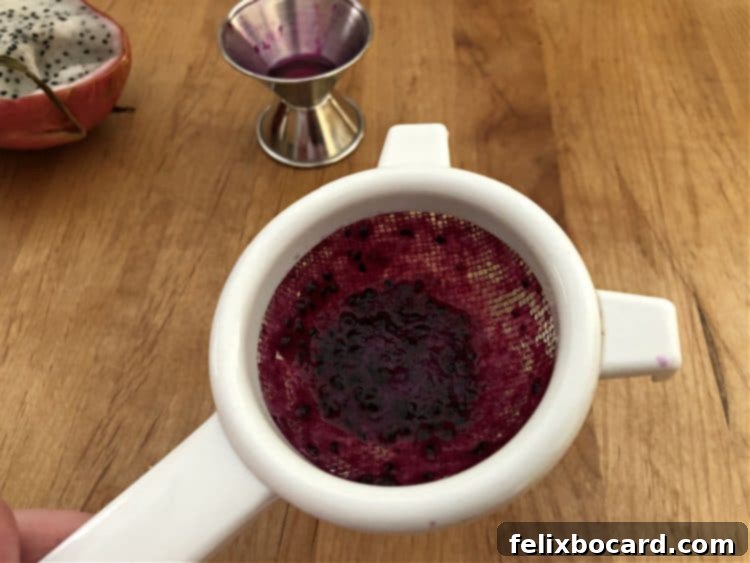 A small mesh strainer being used to double strain a cocktail, capturing pulp and seeds.