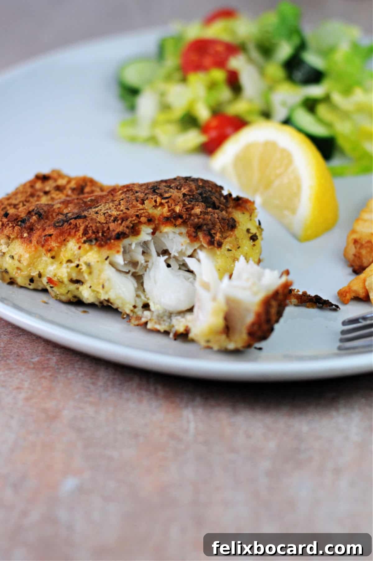 A fork breaking off a piece of golden potato crusted cod to reveal the tender, cooked white fish inside.