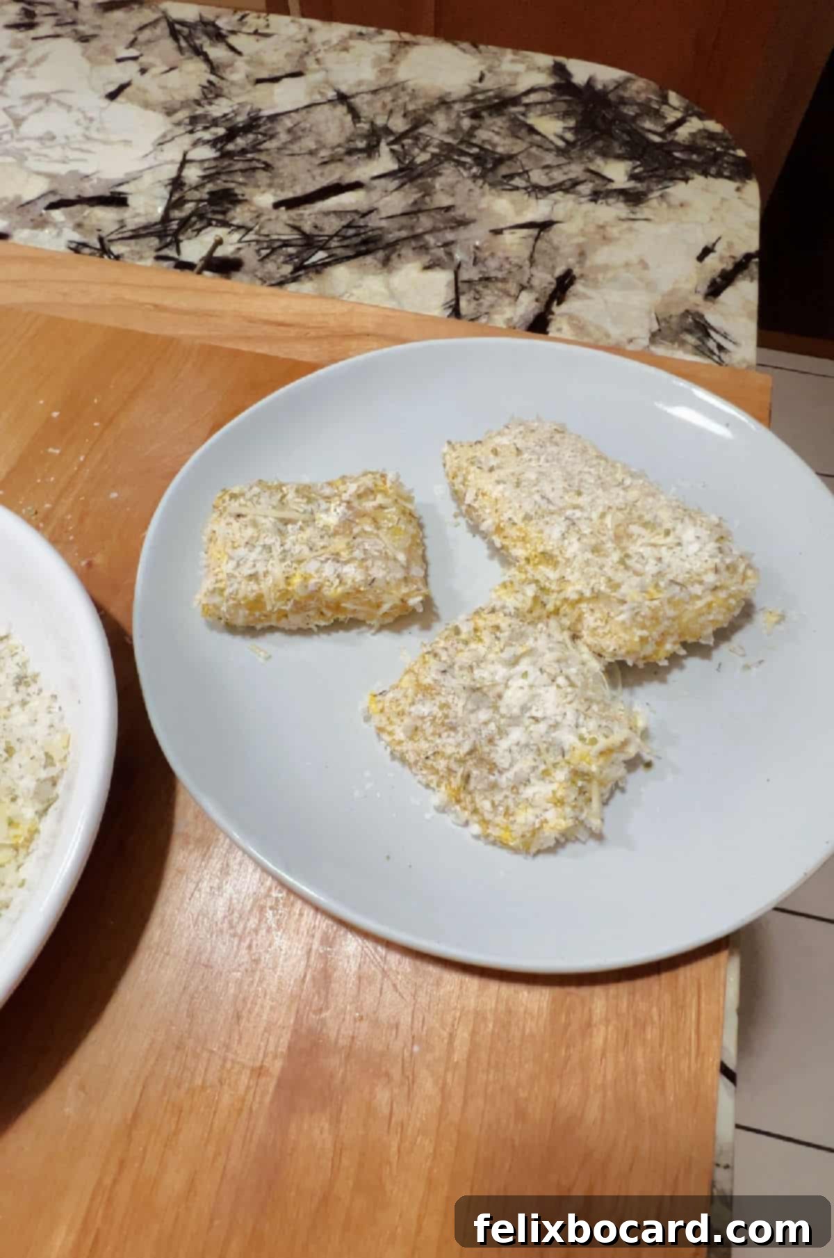 Three perfectly coated pieces of cod, ready for cooking, resting on a white plate.