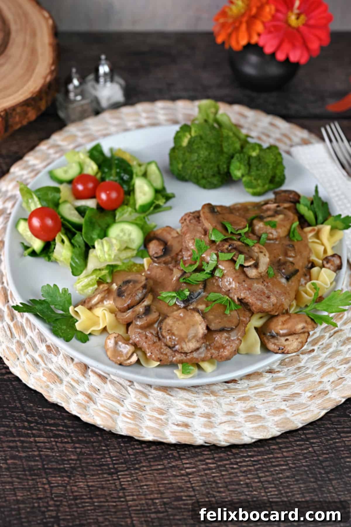A plate with Instant Pot Cube Steak and gravy over noodles, served with salad and broccoli.
