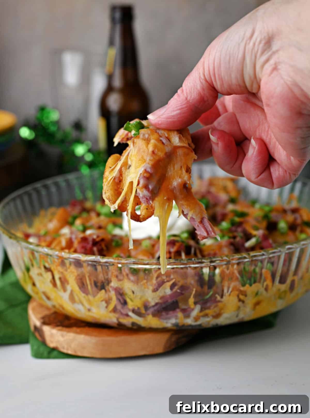 Hand holding some Irish nachos with melted cheese draping down.