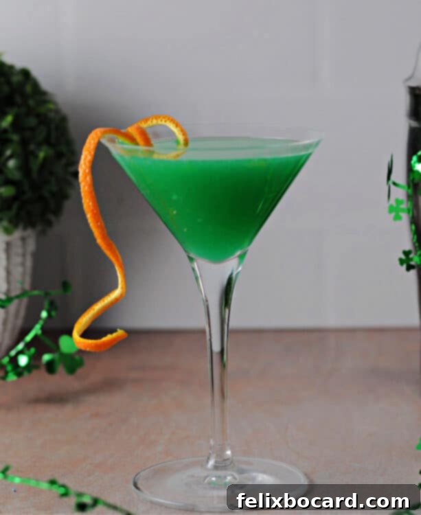 A stunning green Shamrock Martini in a classic martini glass, garnished with a vibrant orange peel, ready for a St. Patrick's Day celebration.