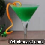 A close-up shot of a vibrant green Shamrock Martini cocktail, garnished with an orange rind, ready to be enjoyed.